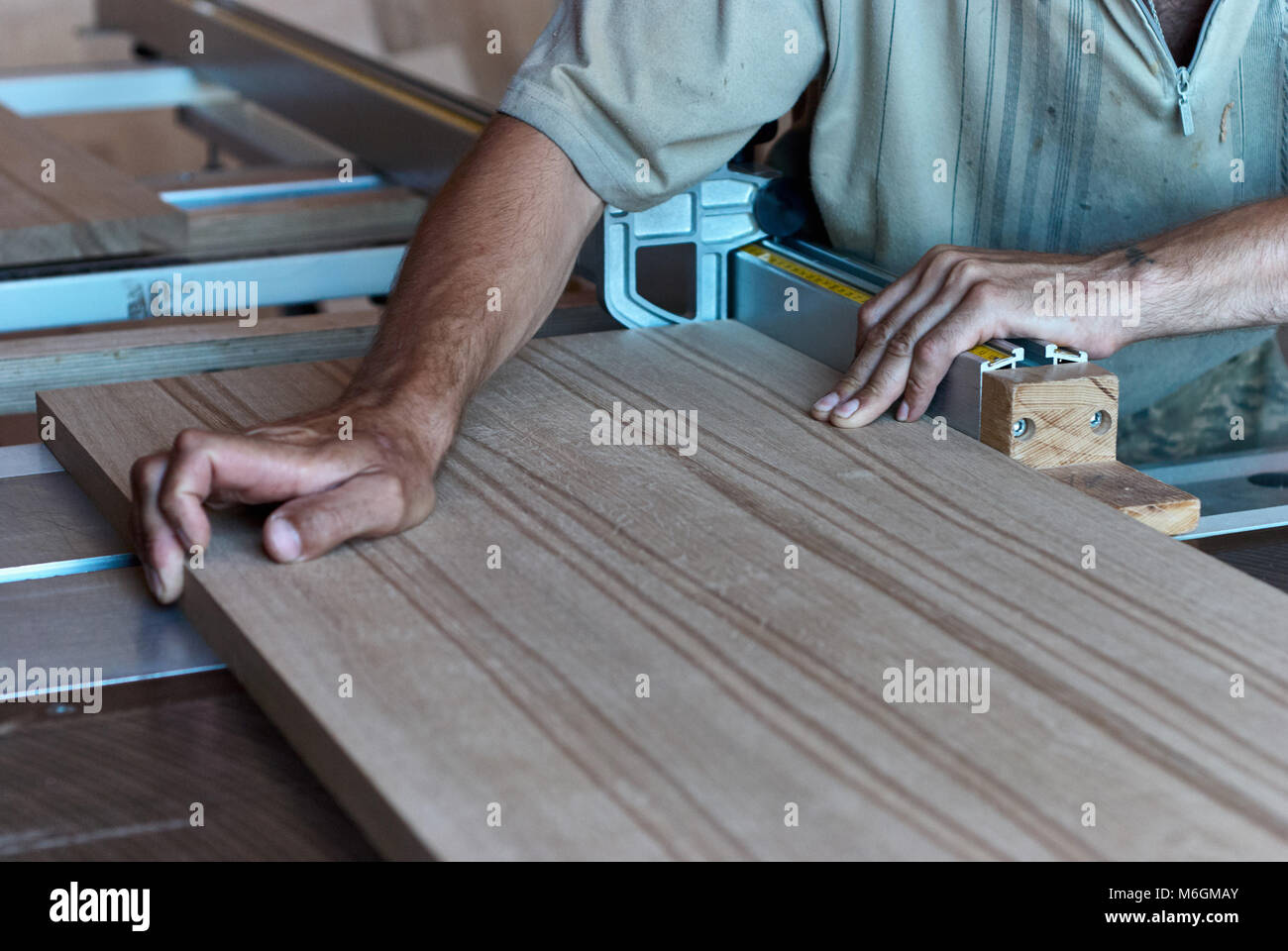 Carpentiere non riconoscibile che utilizza una sega da tavolo affilata per tagliare il pannello in legno incollato durante il lavoro in officina professionale Foto Stock