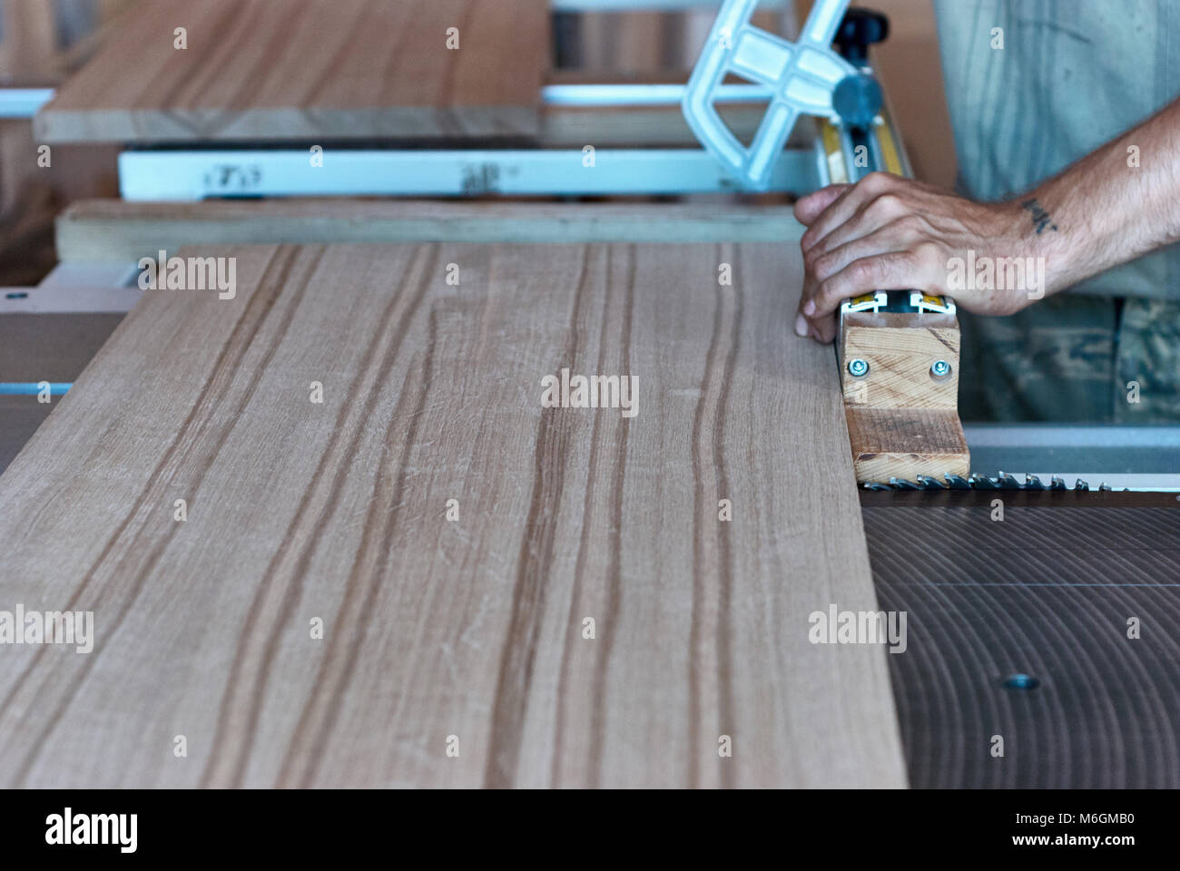 Carpentiere non riconoscibile che utilizza una sega da tavolo affilata per tagliare il pannello in legno incollato durante il lavoro in officina professionale Foto Stock