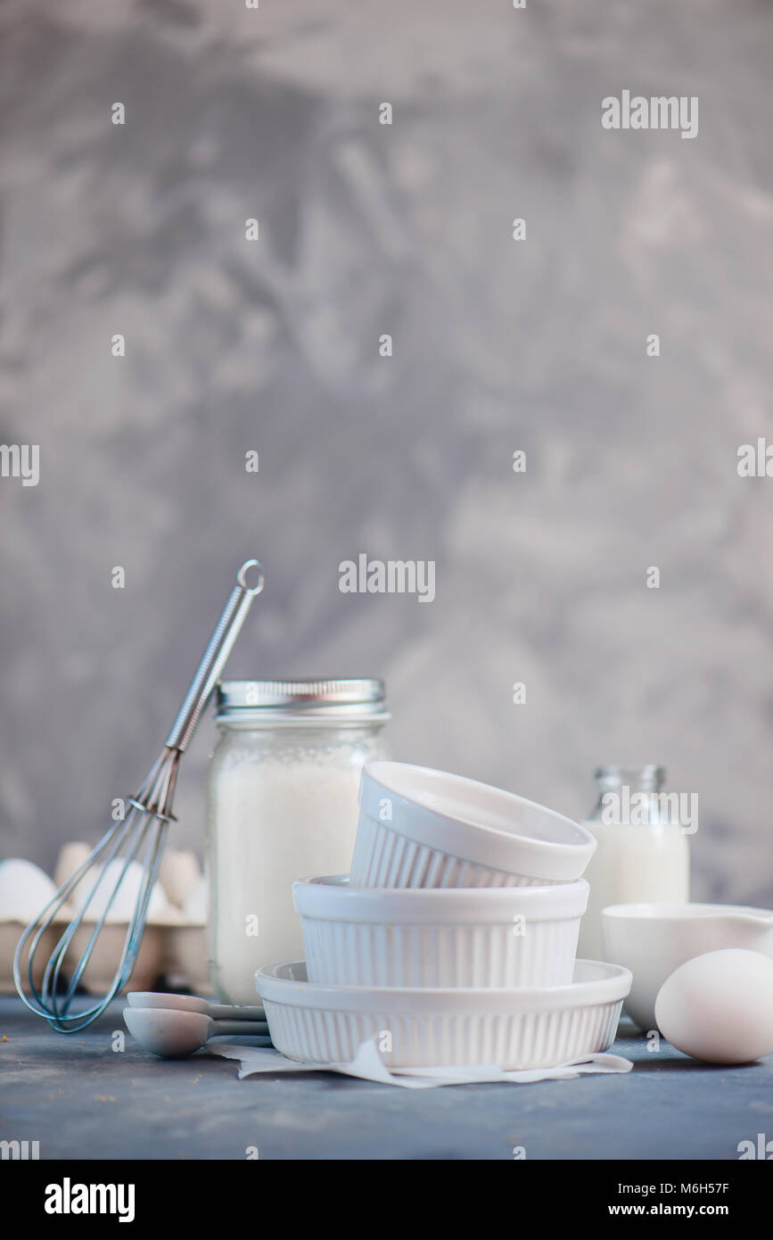 Forme di cottura nel concetto di cucina a vista con le uova, la farina e il latte su un sfondo di calcestruzzo. Elevato La chiave fotografia alimentare con copia spazio. Foto Stock