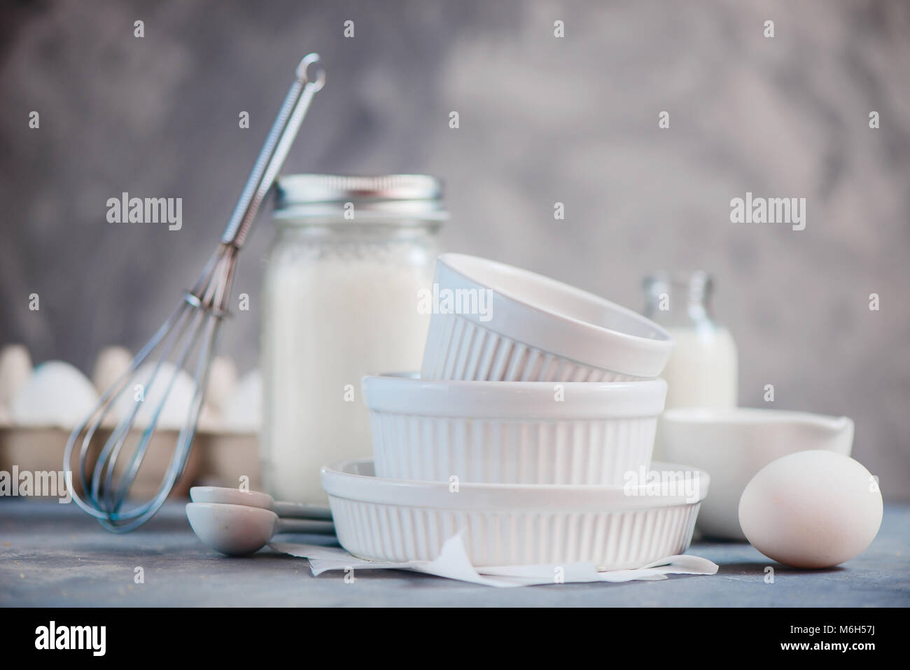 Porcellana forme di cottura nel concetto di cucina a vista con le uova, la farina e il latte su un sfondo di calcestruzzo. Elevato La chiave fotografia alimentare con copia spazio. Foto Stock