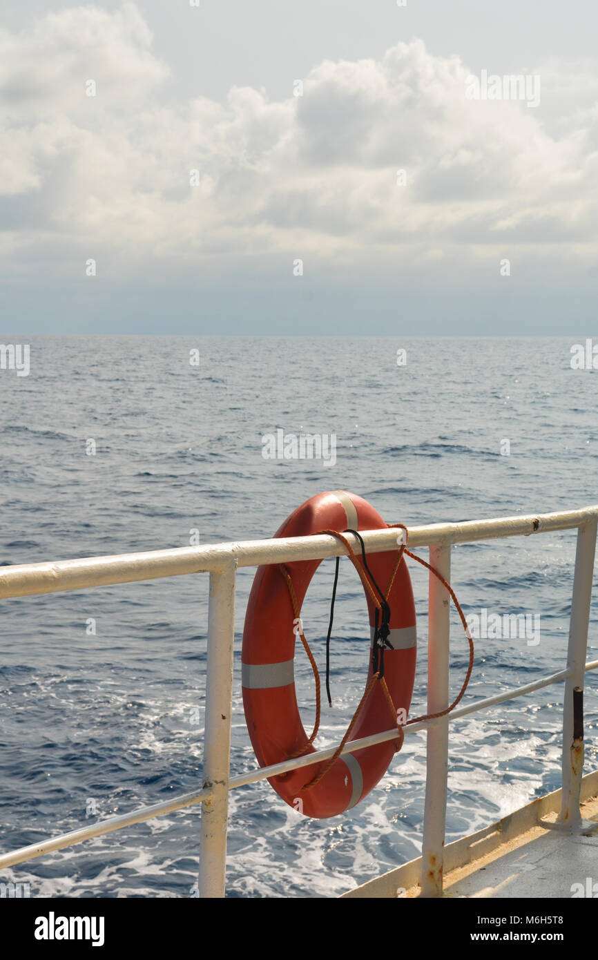Arancione boa di sicurezza appeso sul reiling di una barca in mare sullo sfondo. Foto Stock