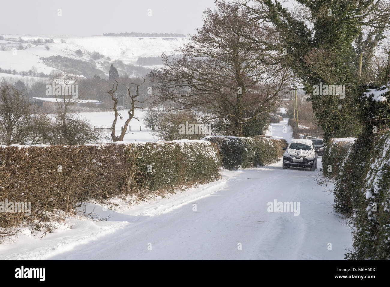 Cars driving in condizioni difficili in un paese di lingua inglese corsia su un nevoso inverno mattina. Foto Stock