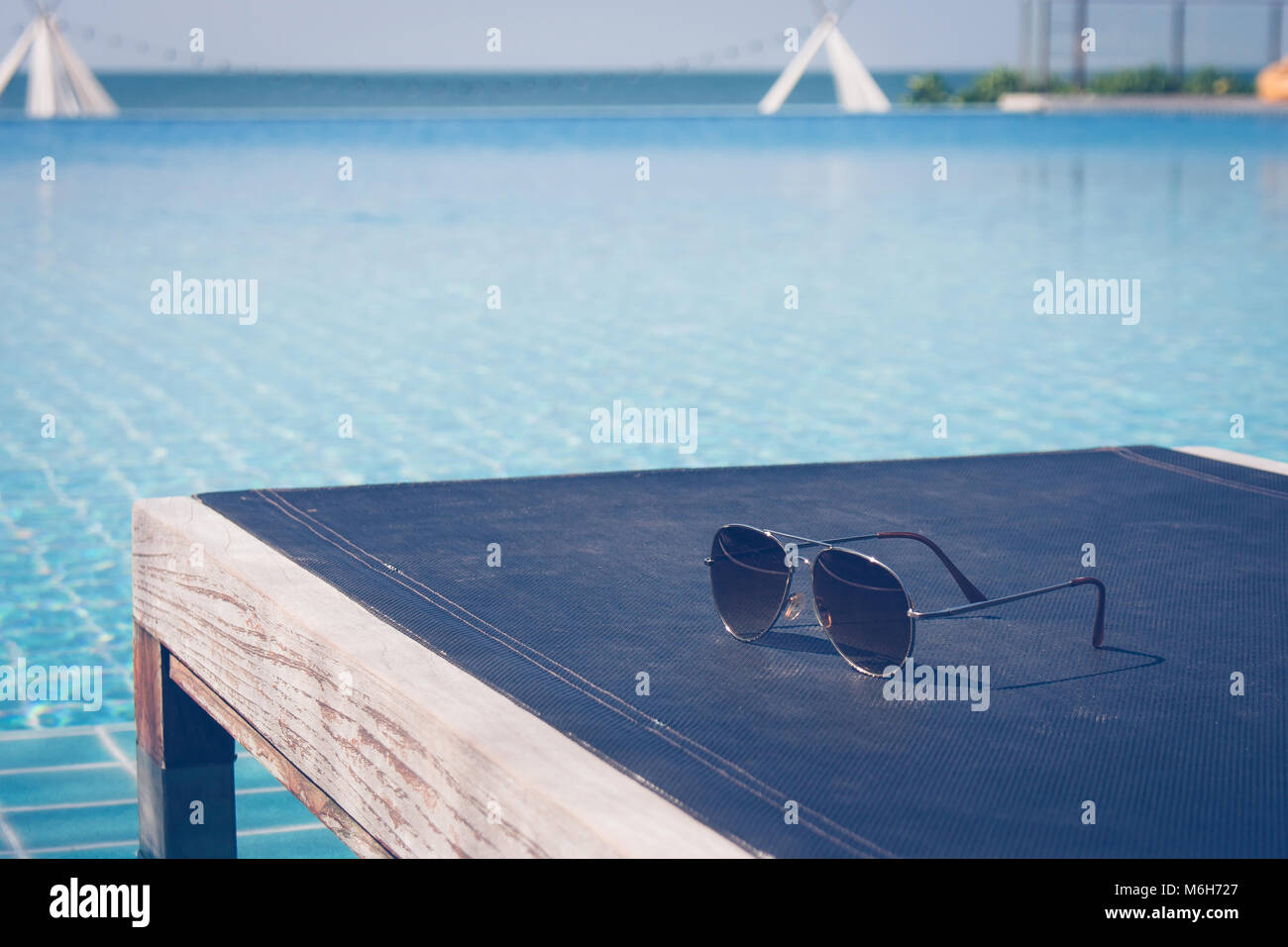 La vacanza estiva e il concetto di Vacanza :Occhiali da sole mettere sul divano letto in legno in piscina con vista seascape in background. Foto Stock