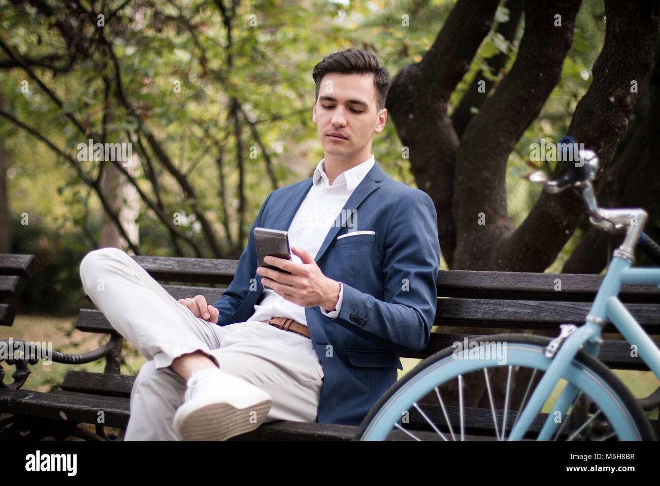Giovane imprenditore seduta su una panchina nel parco, utilizza lo smartphone. Foto Stock