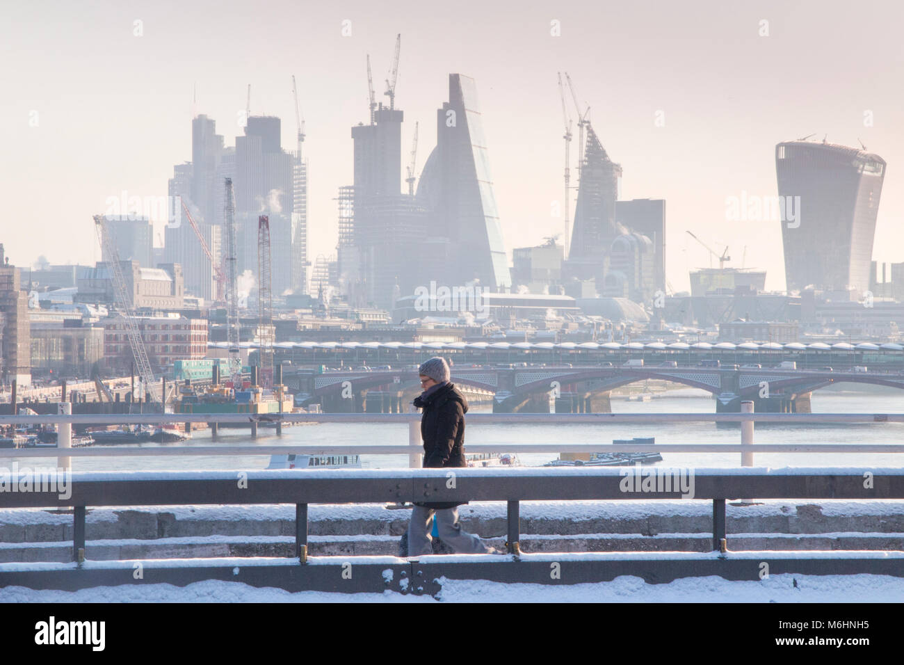 Un " commuter " passeggiate sulla neve coperto Waterloo Bridge con la City di Londra quartieri finanziari di grattacieli, la cattedrale di St Paul e edifici alti Foto Stock