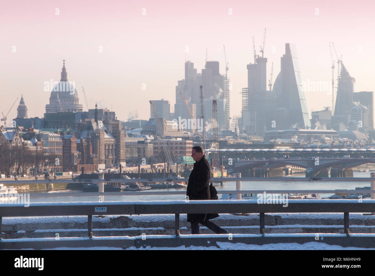 Un " commuter " passeggiate sulla neve coperto Waterloo Bridge con la City di Londra quartieri finanziari di grattacieli, la cattedrale di St Paul e edifici alti Foto Stock