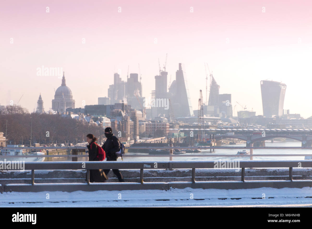 Un " commuter " passeggiate sulla neve coperto Waterloo Bridge con la City di Londra quartieri finanziari di grattacieli, la cattedrale di St Paul e edifici alti Foto Stock