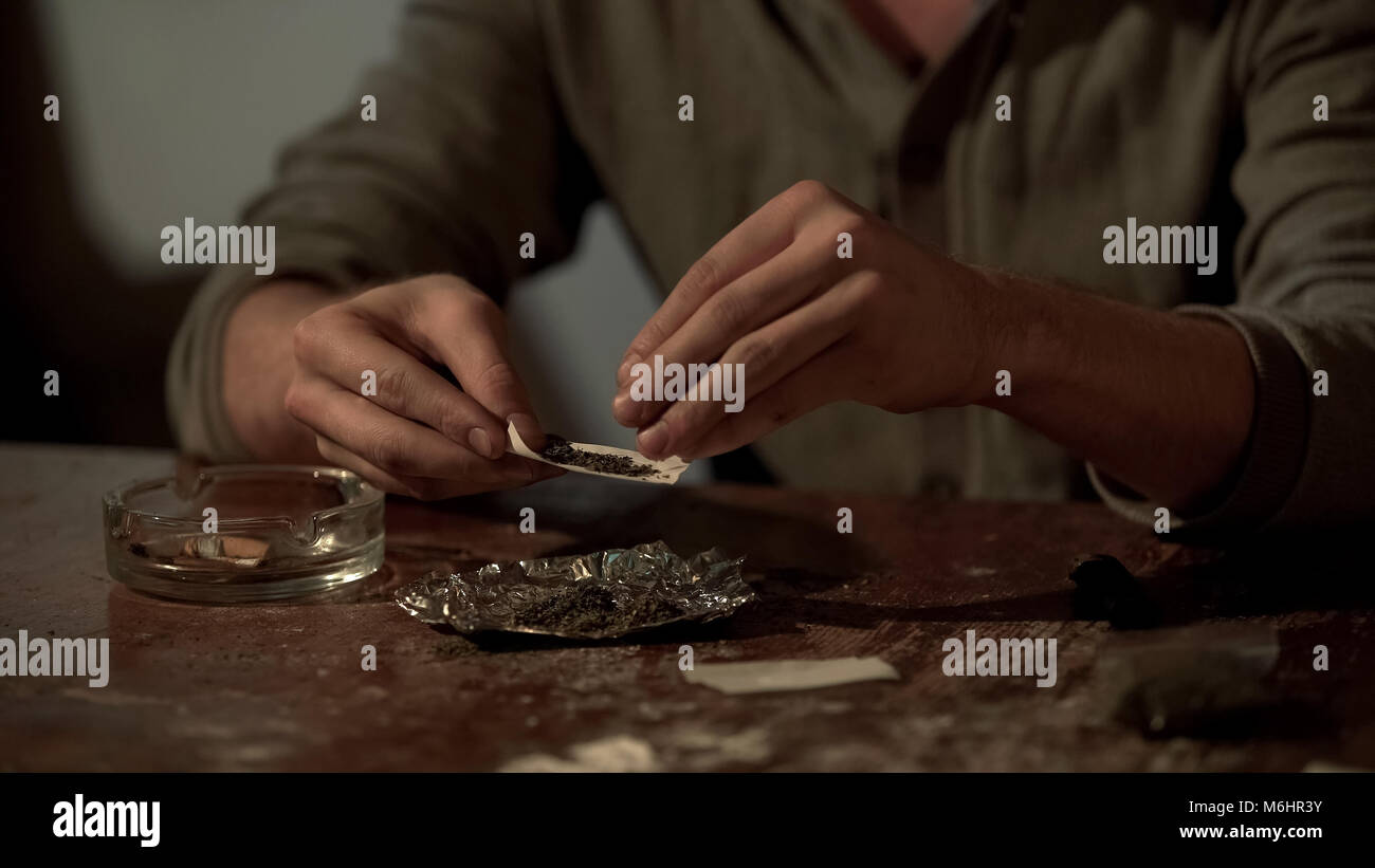 Giovane uomo rendendo sigaretta di cannabis per alleviare lo stress e l abuso di droga psicoattiva Foto Stock
