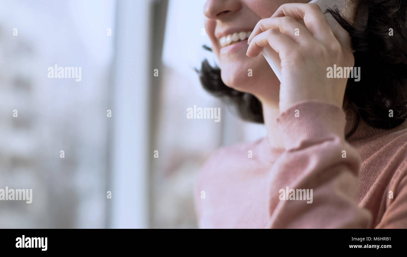 Donna sorridente durante una conversazione su cellulare, finestra in background Foto Stock