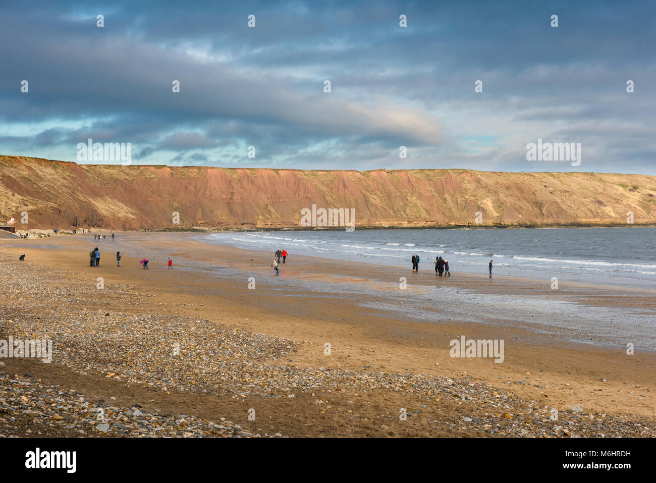 Yorkshire spiaggia inverno, vista di gente camminare sulla spiaggia in Filey Bay con le scogliere noto come Filey Brigg in background,Yorkshire, Inghilterra, Regno Unito Foto Stock