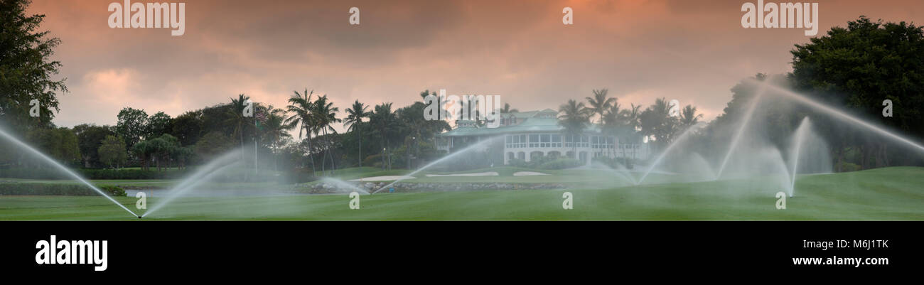 Bellissimo tramonto tropicale al campo da golf scenic panorama, clubhouse privato palme lago, soft focus attraverso gli sprinkler crea pacifica atmosfera rilassata Foto Stock