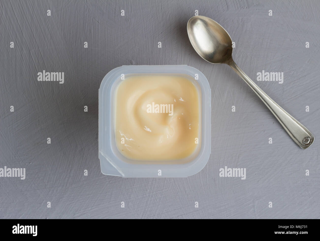 Sana frutta pesche yogurt aromatizzati con colorazione naturale in una tazza di plastica isolati su grigio Sfondo texture con piccolo cucchiaio d'argento - close up top v Foto Stock