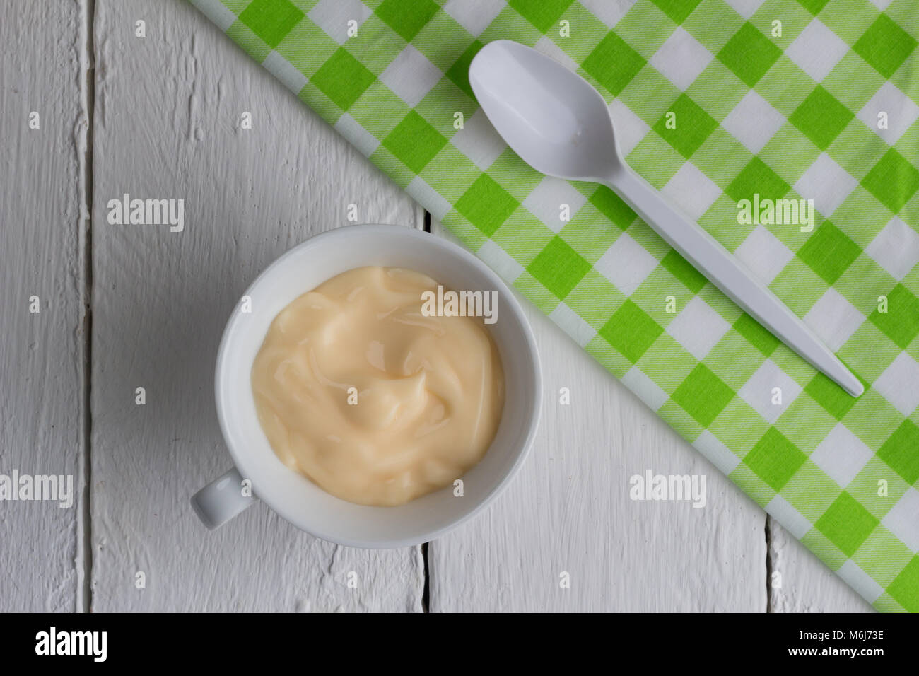 Una sana peach / albicocca frutta yogurt aromatizzati con colorazione naturale in piccola tazza bianca isolata su bianco tavolo in legno con uno sfondo bianco di piccole dimensioni pla Foto Stock
