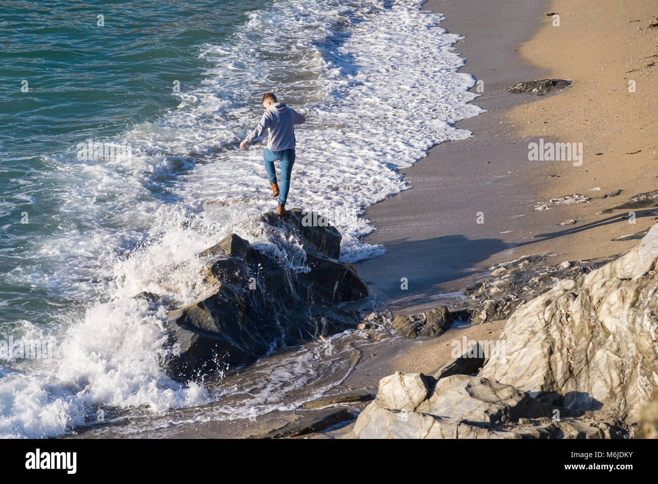 Un giovane uomo di equilibratura su rocce come la marea arriva a poco Fistral Beach in Newquay Cornwall. Foto Stock