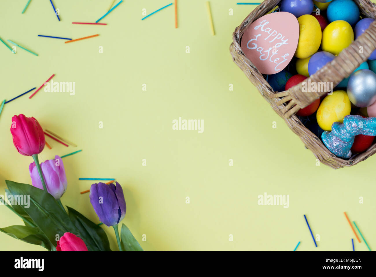 Vista sopra lo sfondo bianco di carta gialla incorniciato con tulipani e uova di Pasqua, intenzionale di spazio di copia Foto Stock