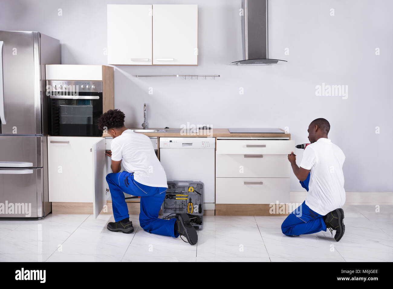 Vista posteriore di due giovani Handymen in uniforme che fissa i cabinet in legno in cucina Foto Stock