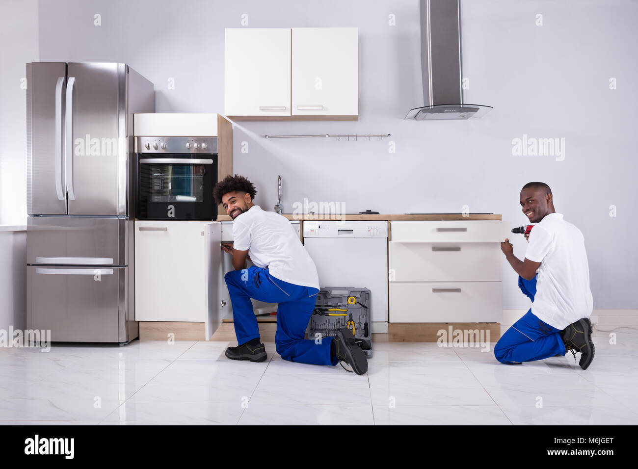 Vista posteriore di due giovani Handymen in uniforme che fissa i cabinet in legno in cucina Foto Stock