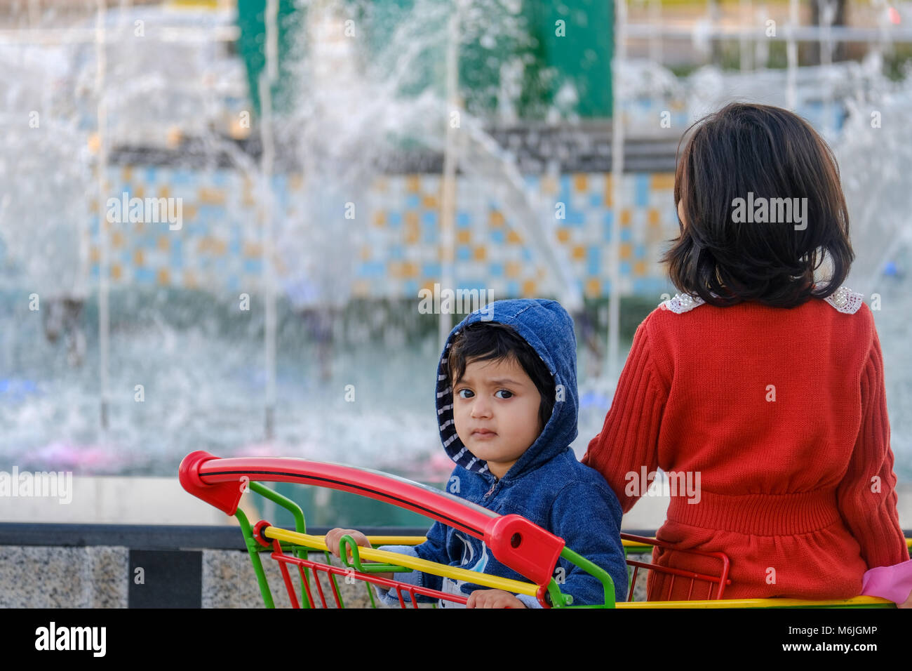 Due asian le piccole bambine in piedi nel Carrello della spesa guardando la fontana nella parte anteriore del Centro Commerciale di Mushrif Foto Stock