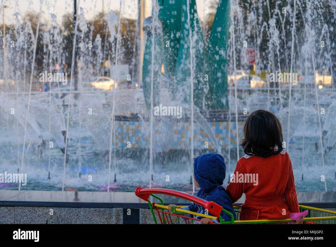 Due asian le piccole bambine in piedi nel Carrello della spesa guardando la fontana nella parte anteriore del Centro Commerciale di Mushrif Foto Stock
