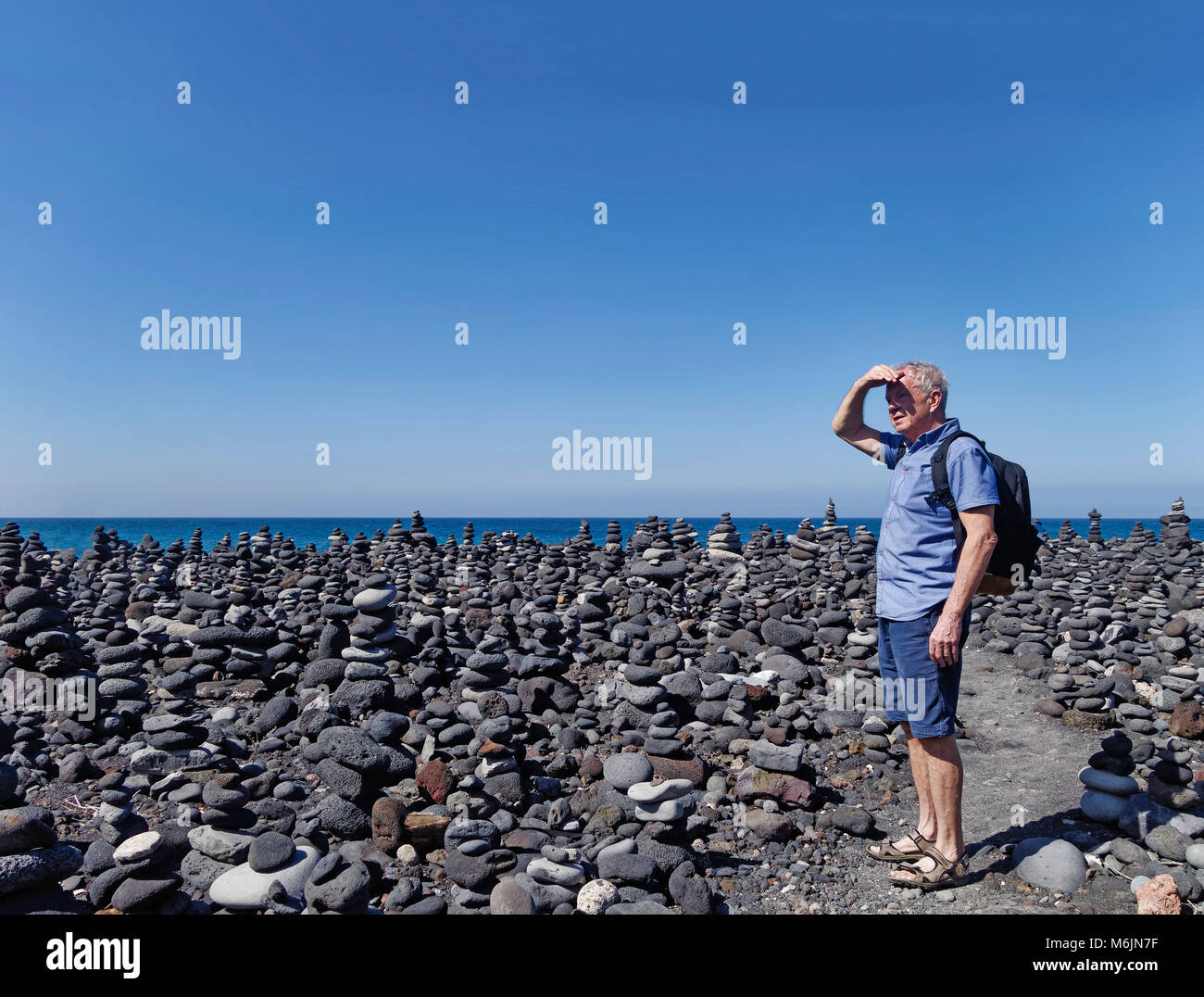 Uomo anziano che si erge tra i cumuli di pietre a Puerto de la Cruz Foto Stock