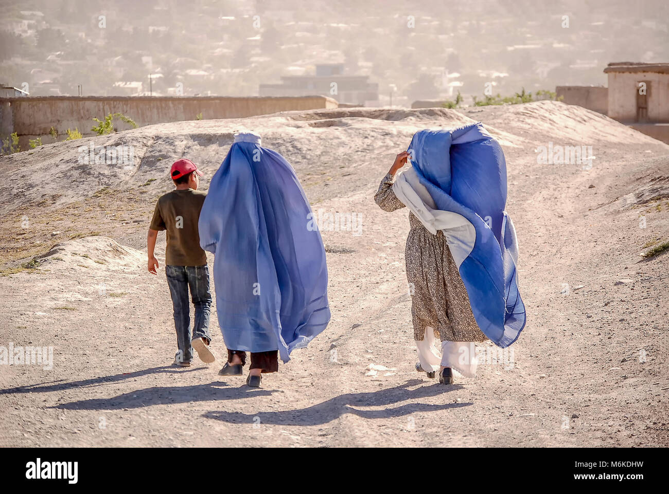 Le donne a piedi in un burka blu su una strada sterrata con un bambino con un vestito che mostra a Kabul in Afghanistan Foto Stock