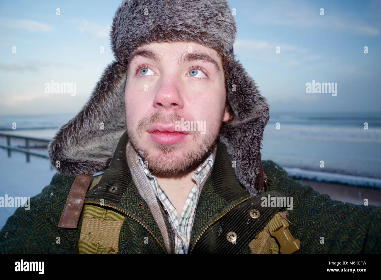 Attraente Giovane Uomo nel lusso abbigliamento invernale sulla neve spiaggia di Aberdeen, bombardiere Hat e giacca di tweed. La Scozia, Regno Unito. Foto Stock
