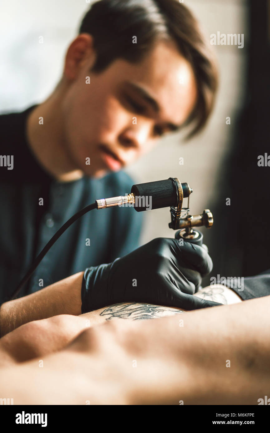 Tatuaggio artista maschile rende un tatuaggio su una gamba femminile. Foto Stock