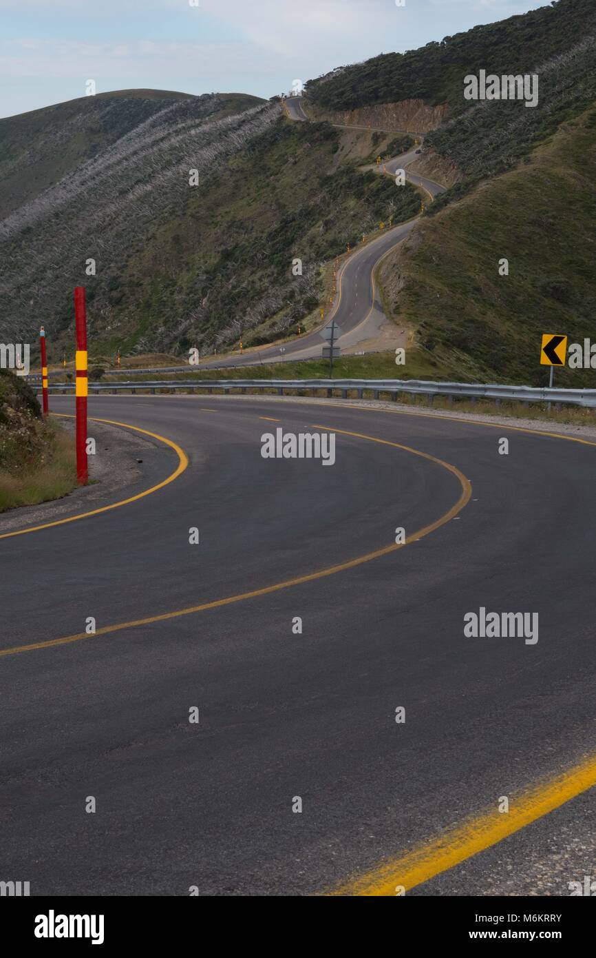 Avvolgimento di due corsie attraverso australiano regione delle Alpi con strisce gialle, segni di curva di rosso le racchette da neve e di dolci colline e montagne arrotondate Foto Stock