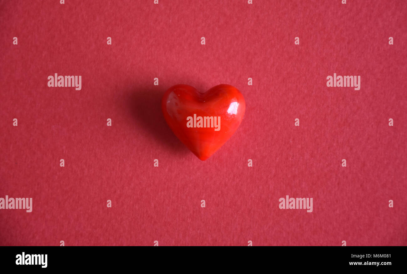 Piccolo rosso amore cuore ciottoli contro uno sfondo semplice Foto Stock
