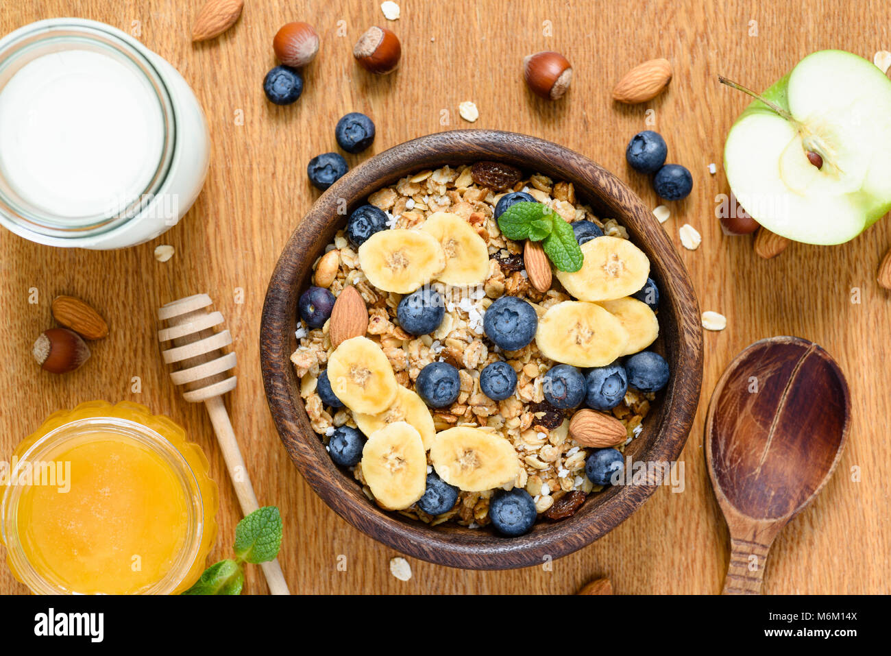 Ciotola di muesli con mirtilli e fette di banana, mela, miele e latte. Tabella vista dall'alto. Concetto di stile di vita sano, mangiare sano, dieta e fitness, v Foto Stock