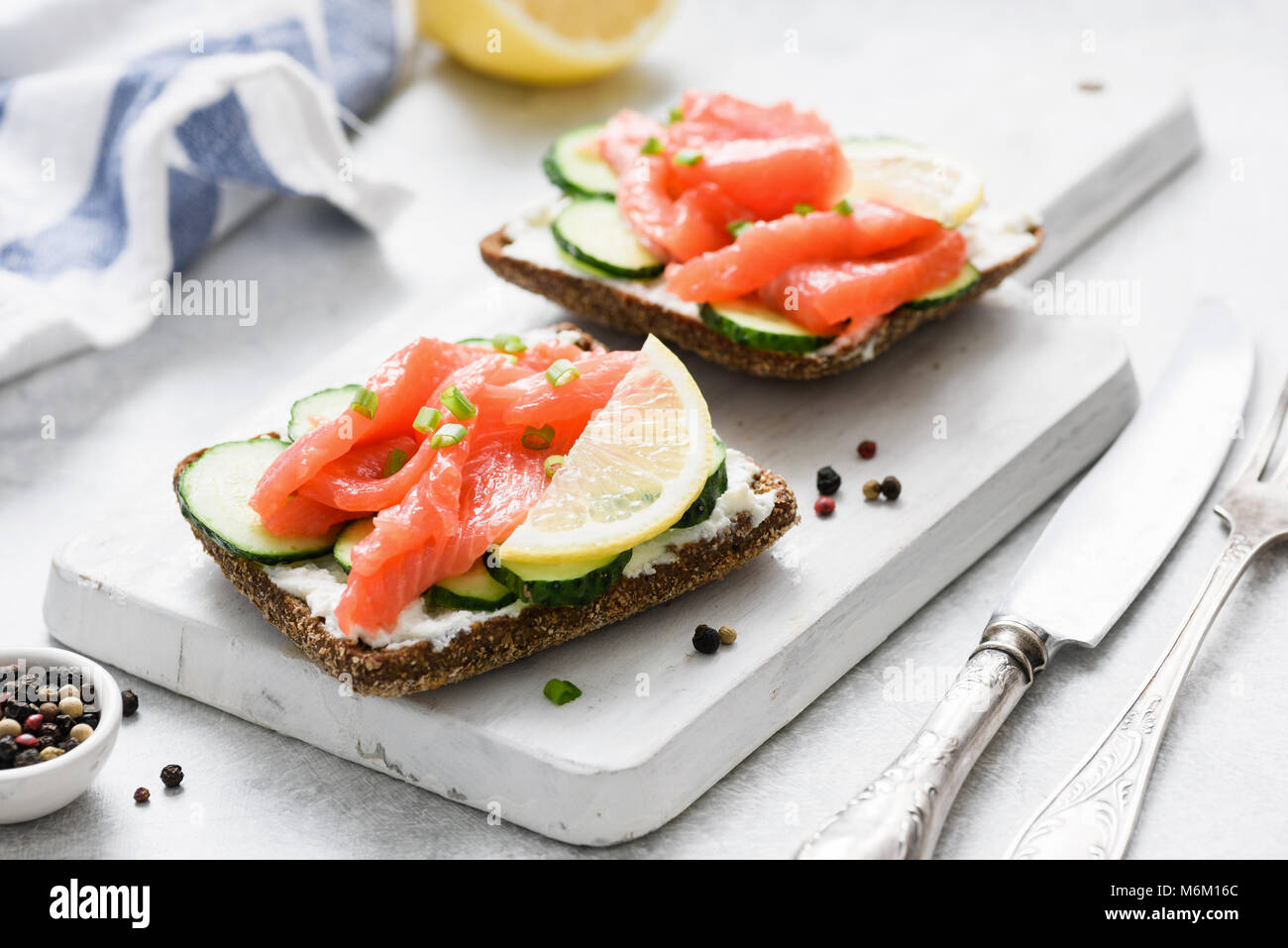 Salmone toast con crema di formaggio e cetriolo su bianco tagliere, primo piano. Snack sani, antipasto o prima colazione Foto Stock