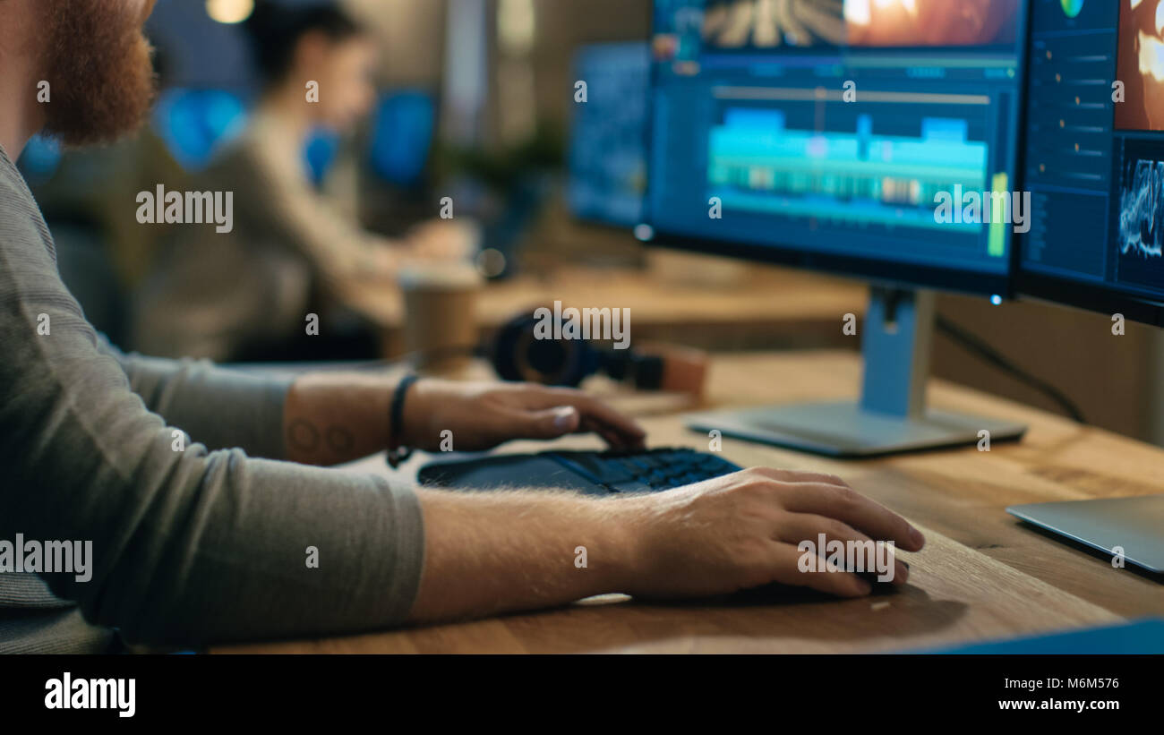 Videografo maschio modifiche e tagli di filmati e audio sul suo personal computer con due schermi. Il suo ufficio è moderno e creativo Studio Loft. Foto Stock