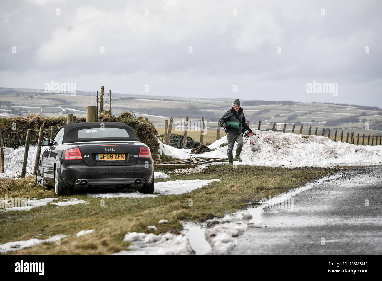 Un uomo ritorna alla sua vettura ha abbandonato sulla A39, Exmoor, vicino a Lynton, a causa del recente maltempo, come la strada resta chiusa a causa della neve. Foto Stock