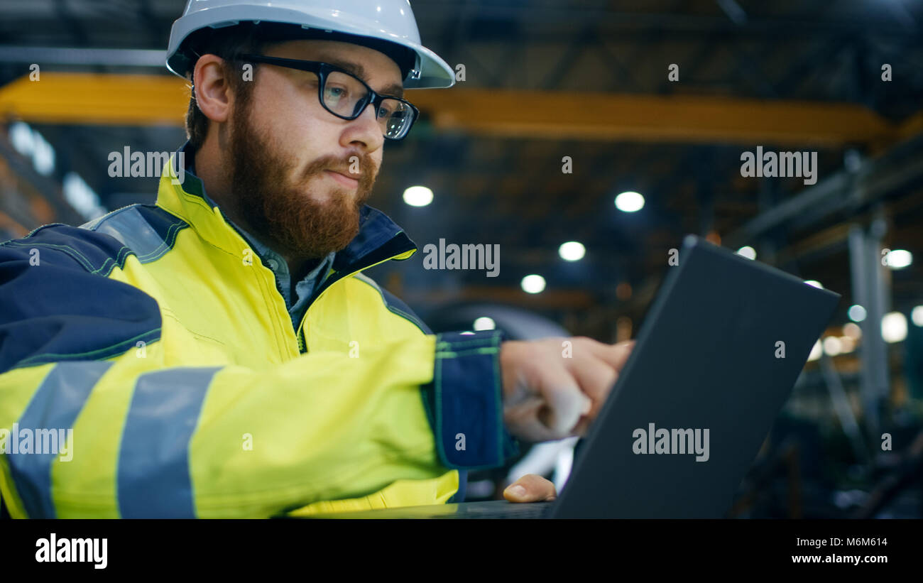 Ingegnere Industriale in Hard Hat indossando giacca di sicurezza utilizza il touchscreen portatile. Lui lavora all'industria pesante Manufacturing Factory. Foto Stock