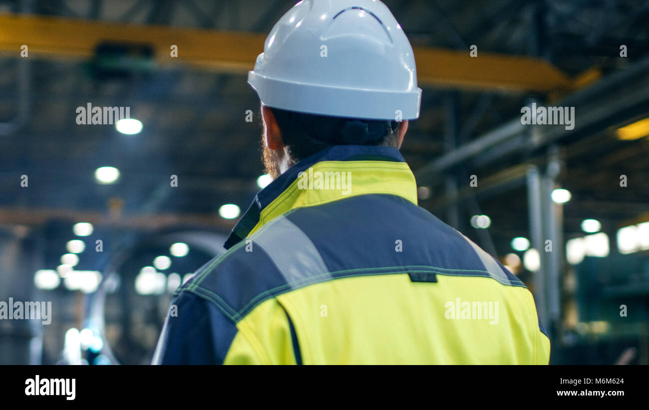 Ingegnere Industriale in elmetto e giacca di sicurezza si guarda intorno nella grande industria pesante Manufacturing Factory. Foto Stock