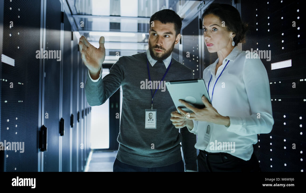 Due tecnici IT nel Data Center / sala server, parlare, uno di loro rivolto in avanti, altri detiene il computer Tablet. Foto Stock