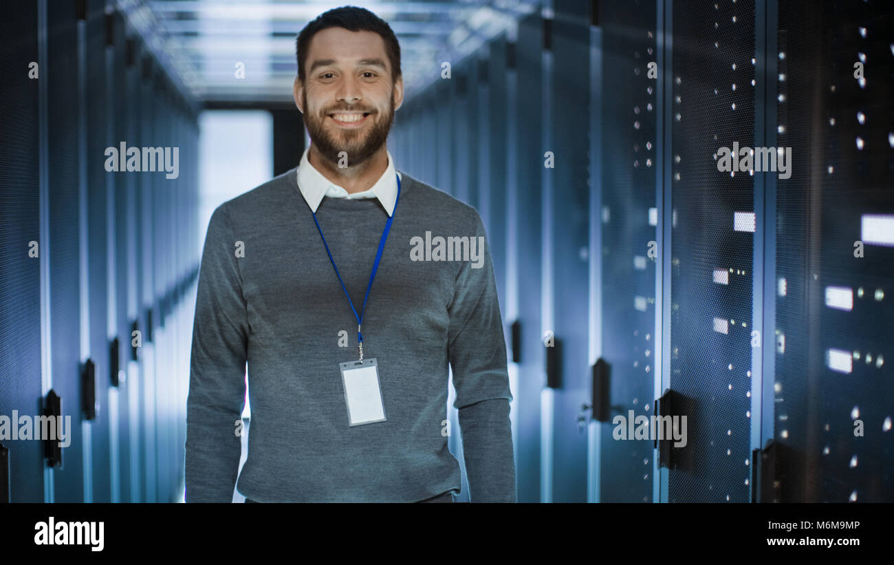 Ritratto di un ingegnere, egli sorride e incrocia le braccia sul petto. Sta lavorando nel centro dati pieno di server Rack. Foto Stock
