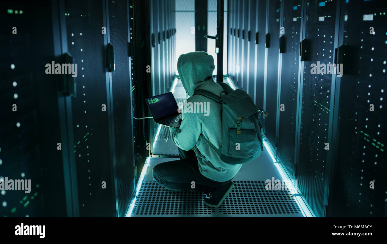 Hacker con il computer portatile si connette al server in rack e ruba le informazioni dai data center aziendali. Foto Stock