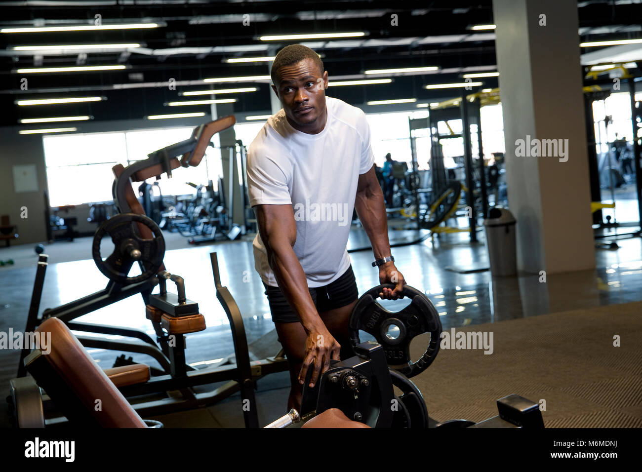 L'uomo africano modifica pesi sulla macchina ginnica Foto Stock