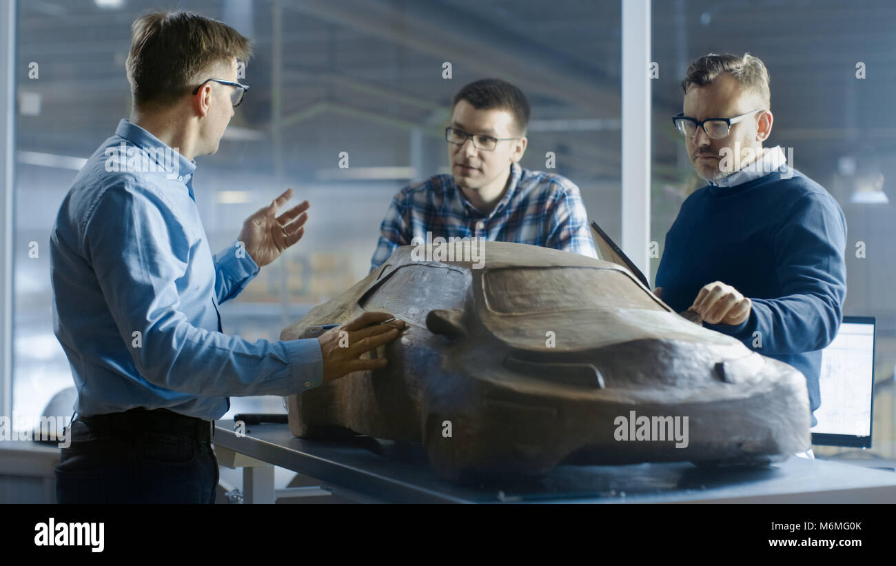 Il team di design automobilistico ingegneri discute un nuovo prototipo di modello fatto di plastilina Clay. Essi lavorano in una grande fabbrica di automobili. Foto Stock