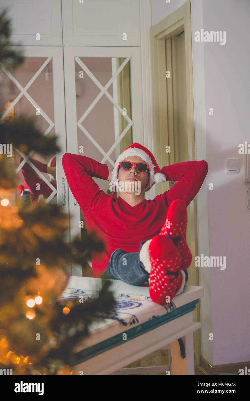 Uomo con Babbo Natale cappello, occhiali da sole e calzini rossi con i suoi  piedi sul tavolo rilassante alla vigilia di Natale a casa sua Foto stock -  Alamy