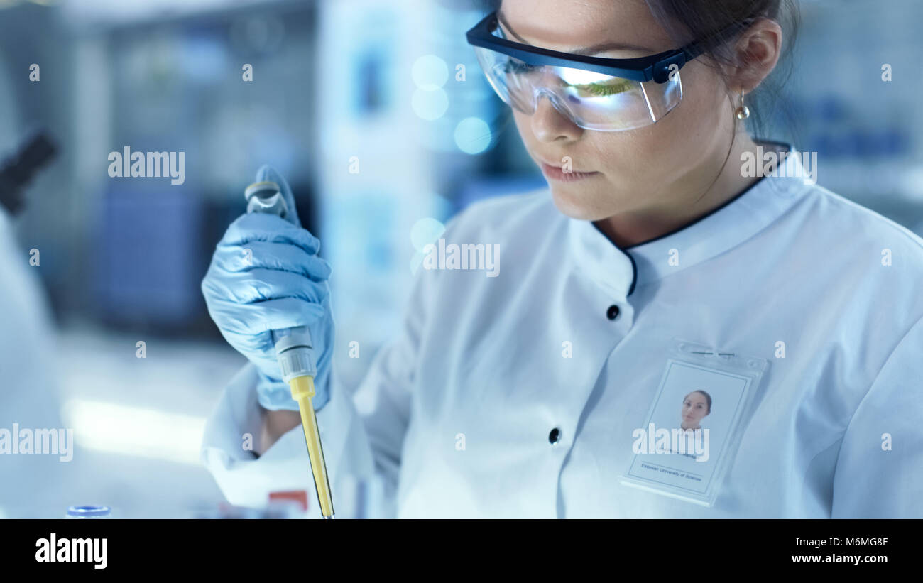 Ricerca di donne scienziato utilizza micropipetta riempire le provette per la prova in un grande e moderno laboratorio. Sullo sfondo gli scienziati stanno lavorando. Foto Stock