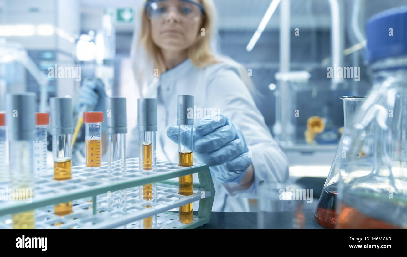 Inquadratura di un carrello con Test-Tubes, analisi, bicchieri e vari articoli di vetreria. Scienziato prende alcuni Test-Tubes per se stessa. Foto Stock