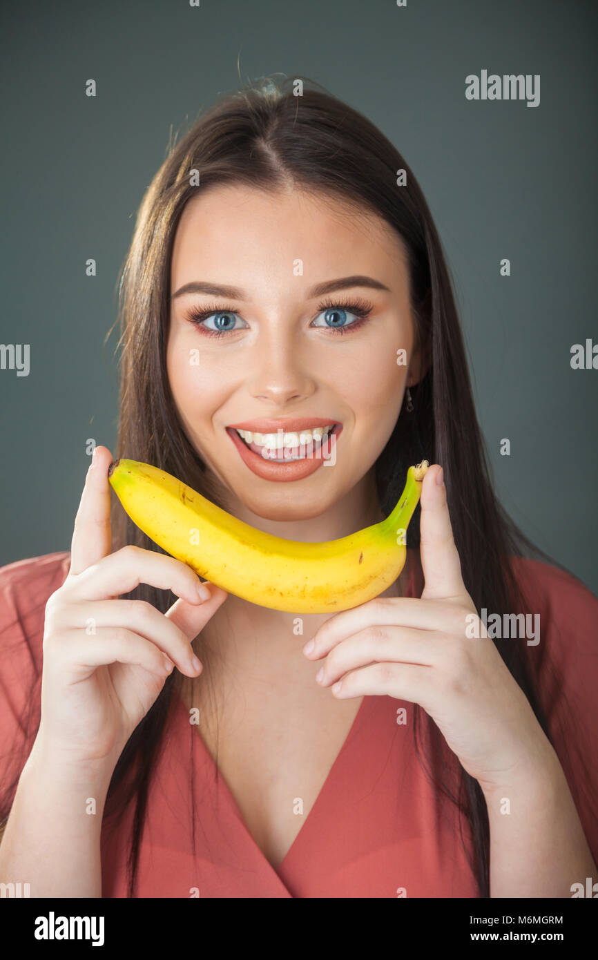 Una bella ragazza adolescente tenendo una banana in entrambe le mani vicino al viso. Foto Stock