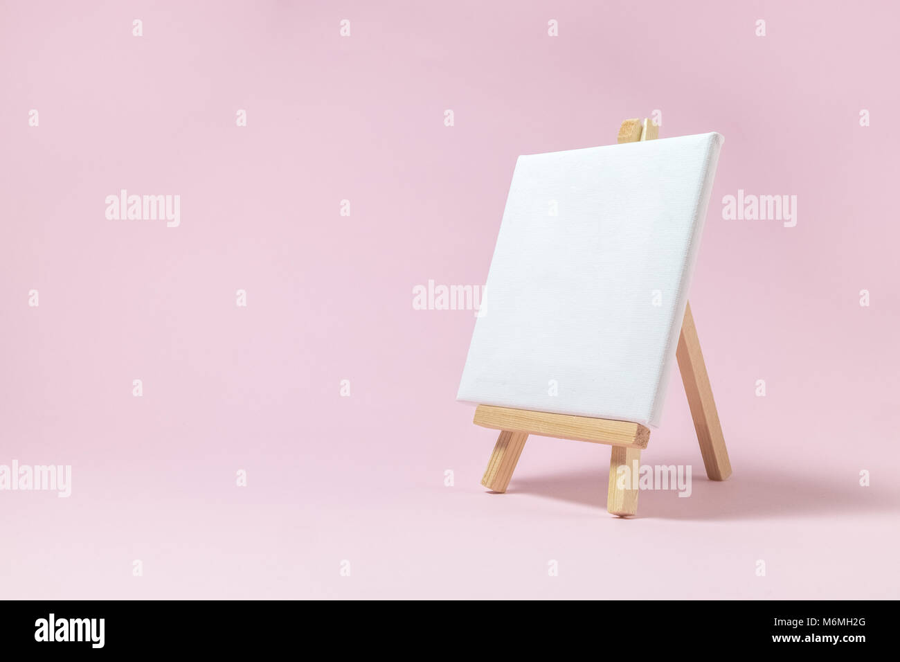 Cavalletto per artisti e tela vuota miniatura su rosa pastello sfondo. Arte la minima nozione. Foto Stock