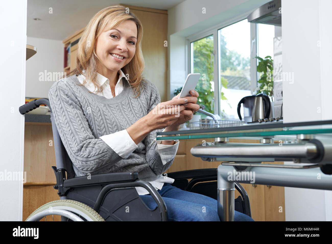 Ritratto di donna disabile in carrozzina tramite telefono cellulare a casa Foto Stock