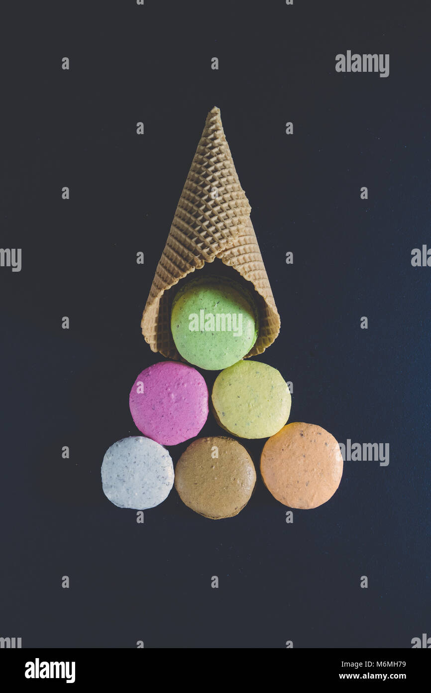 Variopinto macarons cookie e cono di cialda in forma di gelato sfere albero di natale su sfondo nero. La minima nozione Foto Stock