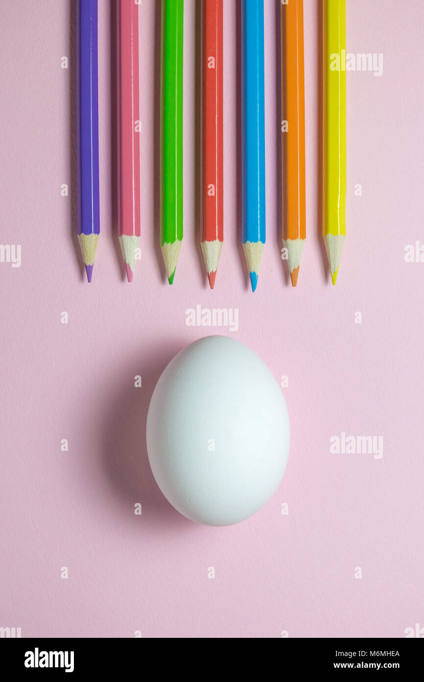 Angolo di alta vista di matite colorate di bianco e di uovo sulla pianura rosa pastello sfondo. La minima nozione di pasqua. Foto Stock