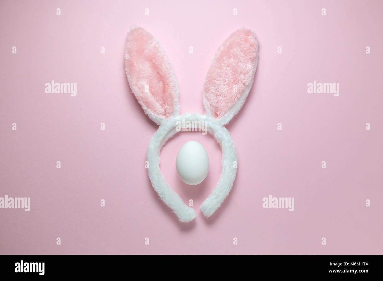 Piatto di laici costume accessorio orecchie di coniglietto bianco e uovo sulla pianura rosa pastello sfondo. Pasqua la minima nozione. Foto Stock