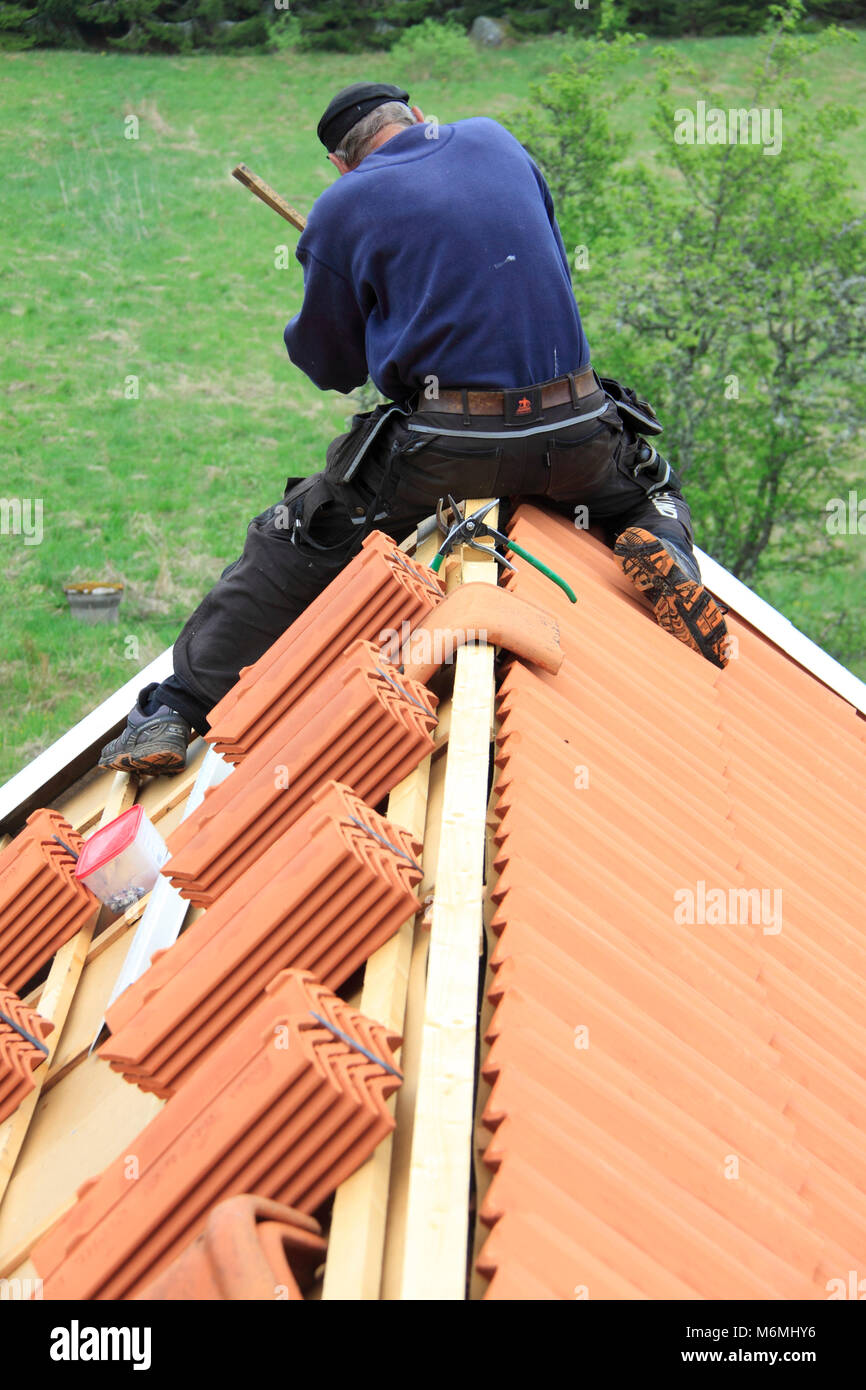 Il lavoro sulla modifica di antiche tegole a quelle nuove. Sul colmo del tetto è un artigiano di fissaggio gronda del tetto di lampeggiare. Foto Stock